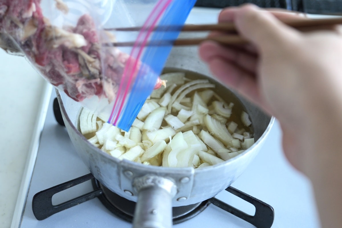 だしにタマネギの薄切りを入れ、マイタケに漬け込んだ牛肉を加え、中火にかけます（写真：筆者撮影）
