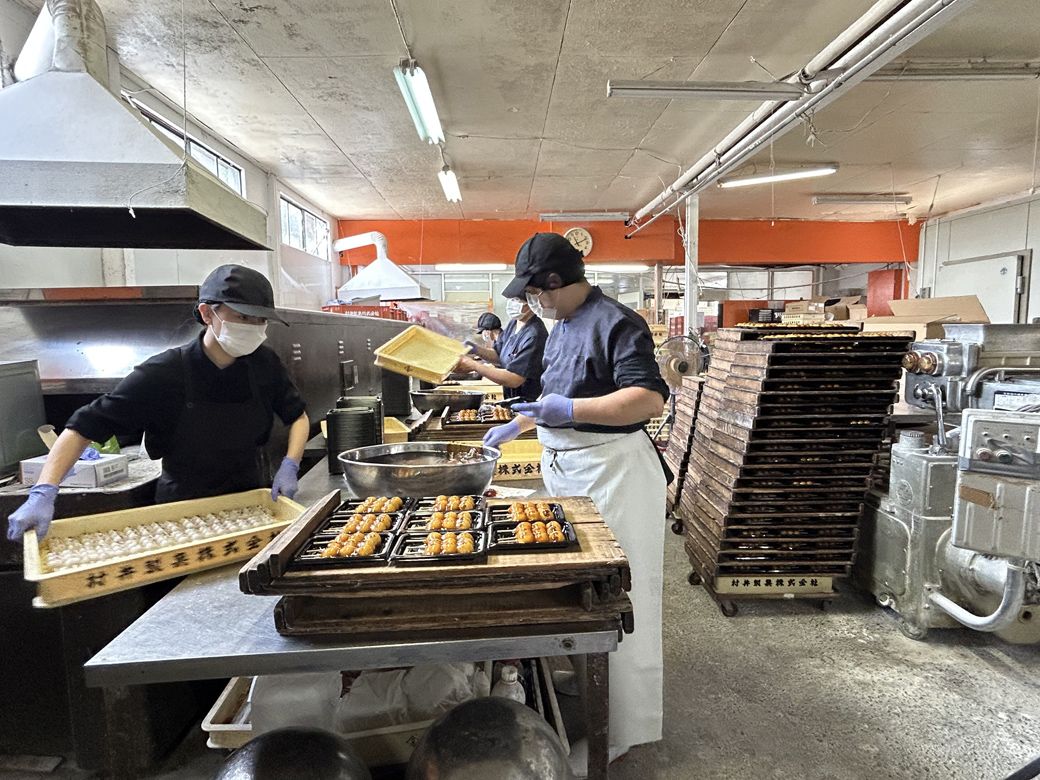 みたらし団子の製造風景。団子にスピーディーにあんをからめていく。年季の入った板がズラリと積み上げられている様は圧巻だ（筆者撮影）