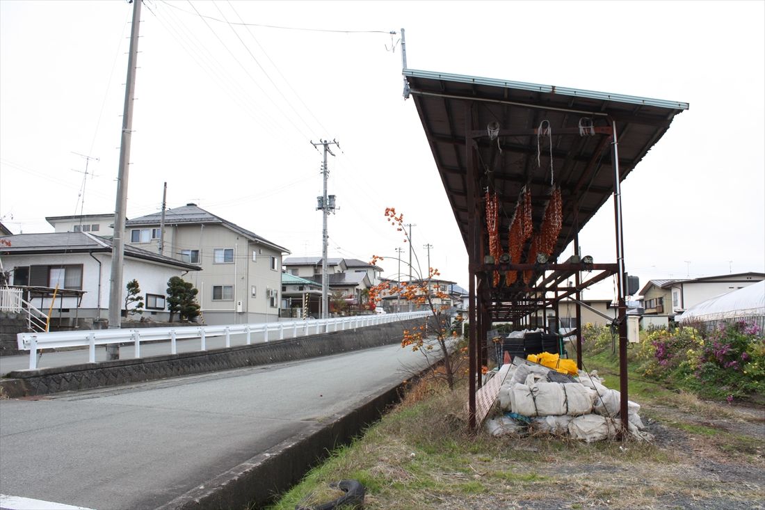 本線と支線の分岐点になるはずだった半郷駅の旧予定地付近。干し柿がつるされた屋根は駅のホーム上屋として建造されたもの……ではなさそうだ（筆者撮影）
