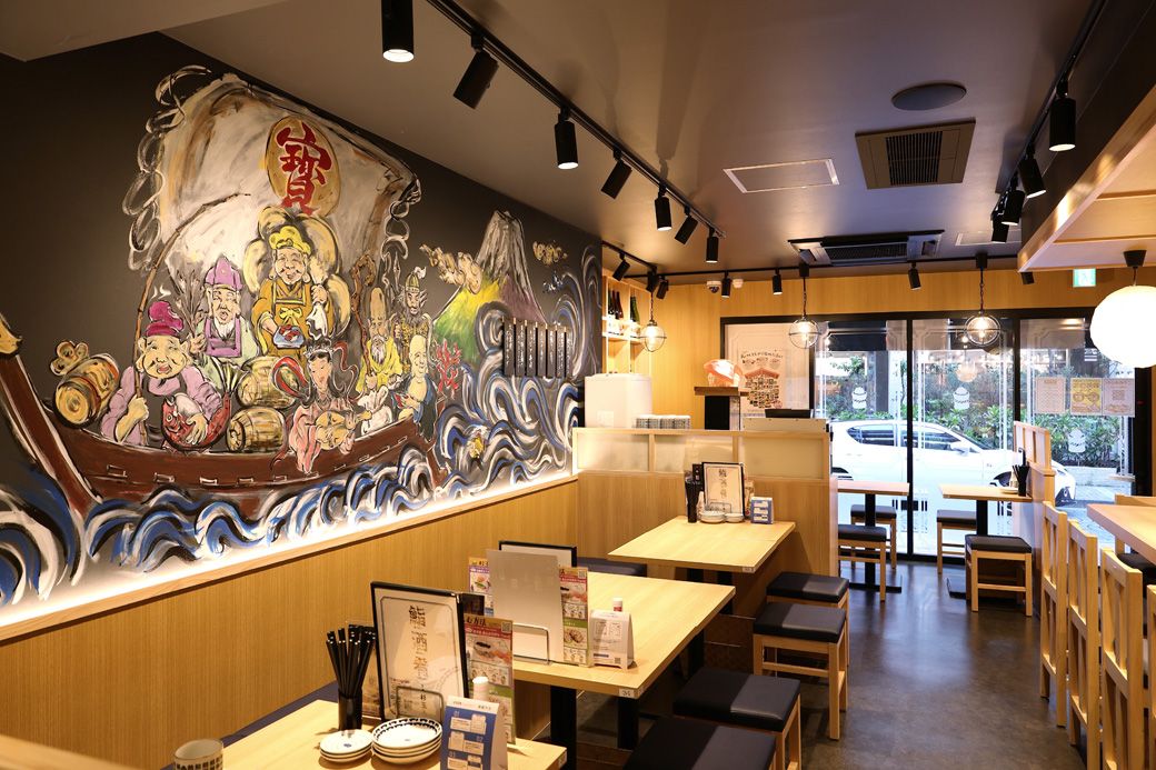 「鮨 酒 肴 杉玉 麻布十番」の店内のようす。幅広い機会、客層を想定し、カウンター、テーブル、ソファ、小上がりなどさまざまなタイプの客席を設えている。全店に描かれた壁画は、両国店なら力士、大船店なら鎌倉の大仏というように、地域性を取り入れていることも（撮影：尾形文繁）