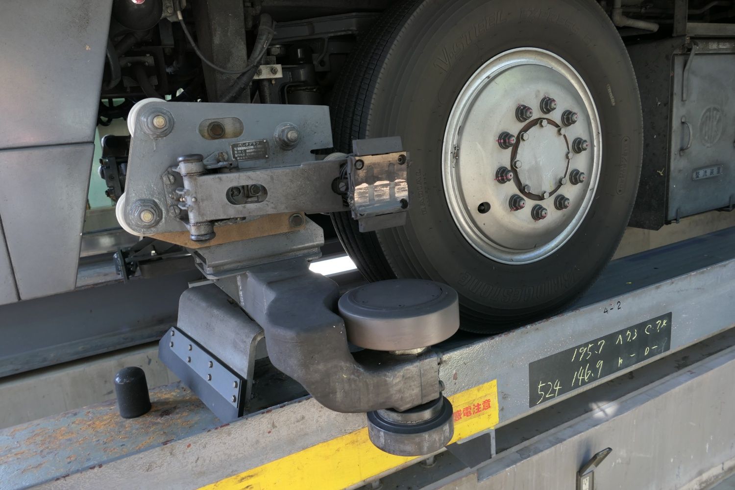 軌道の側面にある架線から電気を取り入れるためのパンタグラフ（中央）。水平の車輪は案内レールに沿って走るための案内輪（記者撮影）