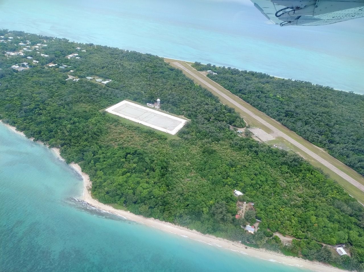 小型飛行機から見たマシッグ島。ほぼ平らだ。中央上部から右下に向かって伸びるのが飛行場の滑走路。左の白い四角い部分は貯水槽。山がなく河川が存在しないため、水は貴重だ（写真：筆者撮影）