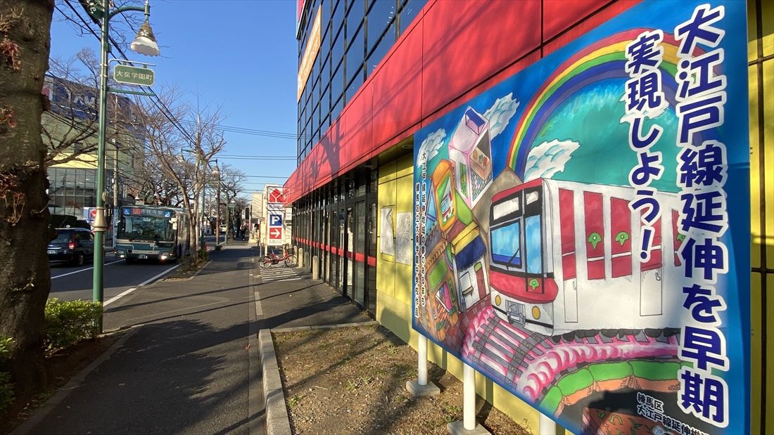 早期延伸実現を訴える看板と、現在の地域の足である路線バス（記者撮影）