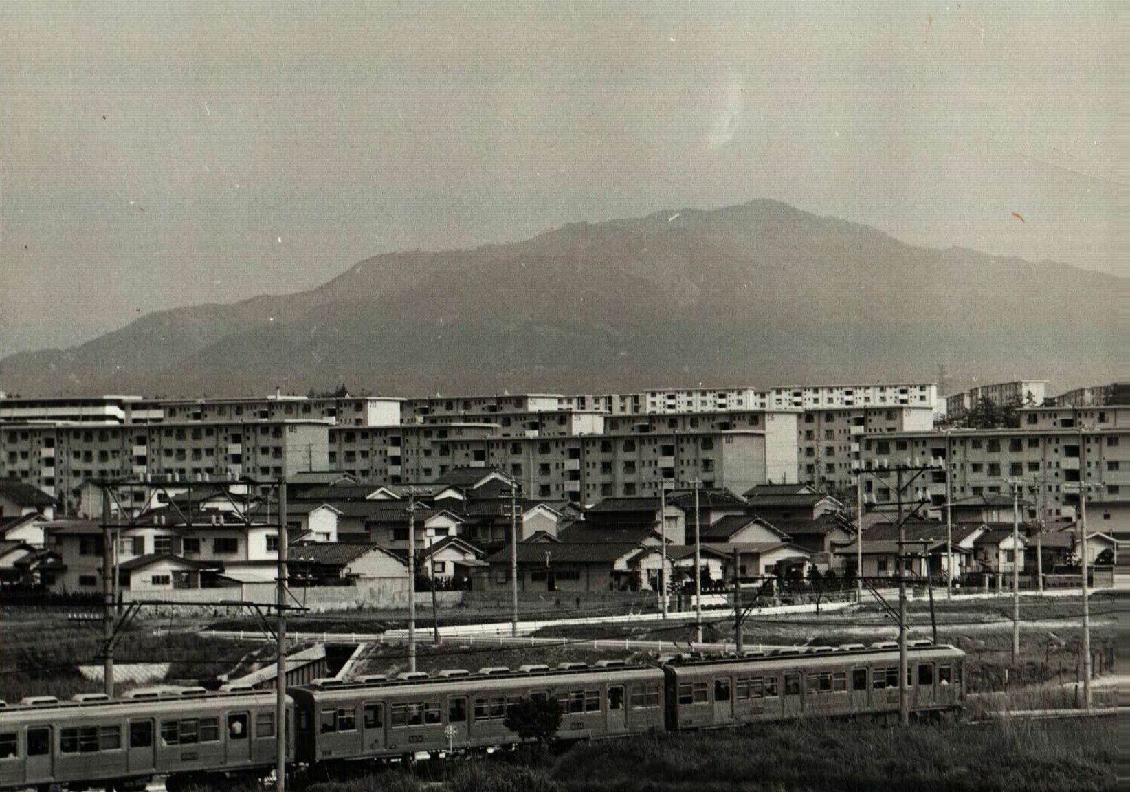 立ち並ぶ団地をバックに走る姿。運転台付きの制御車を中間に連結している（写真：南海電鉄）