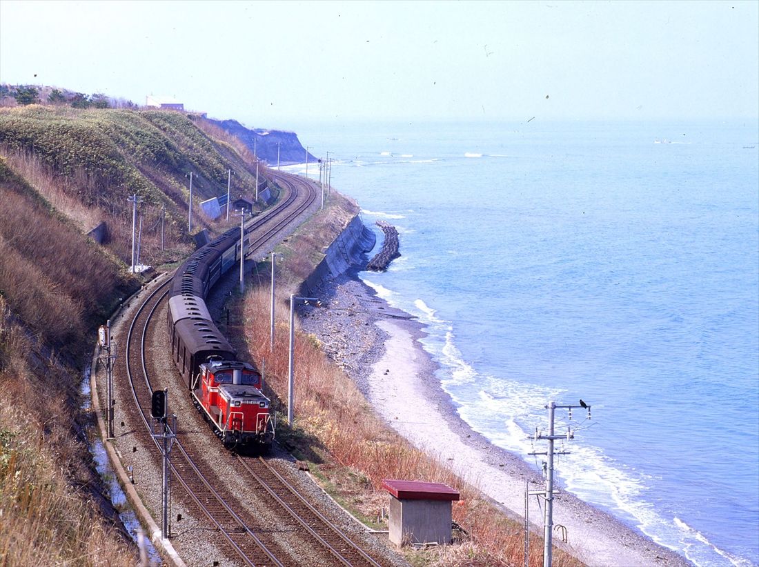 噴火湾沿いの函館本線を、旧型客車を連ねたDD51形牽引の普通列車が走る＝1977年（撮影：南正時）