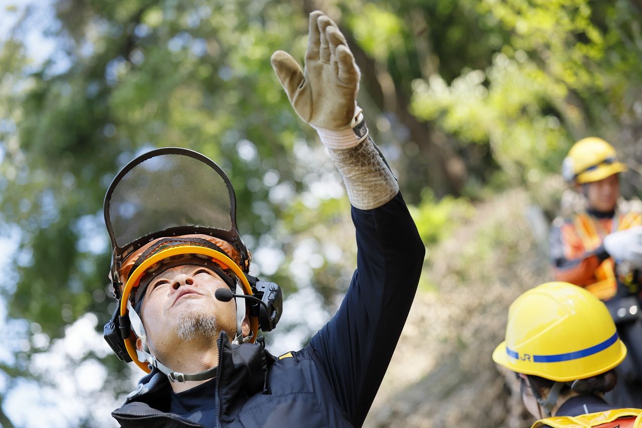 地表にいる監督者は枝をどのように打ち進めたらよいかを脳内で三次元に想像しながら作業者に指示を送る。命綱のほか、切断した枝を吊るロープがあるため、作業者がロープに足を取られないように地上から注意を促す　（筆者撮影）