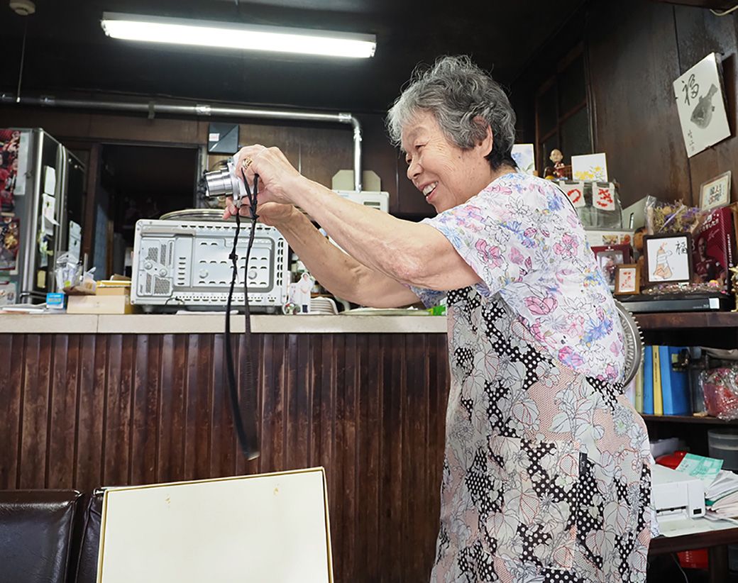 デジカメでお客さんを撮影する紀久恵さん（筆者撮影） 