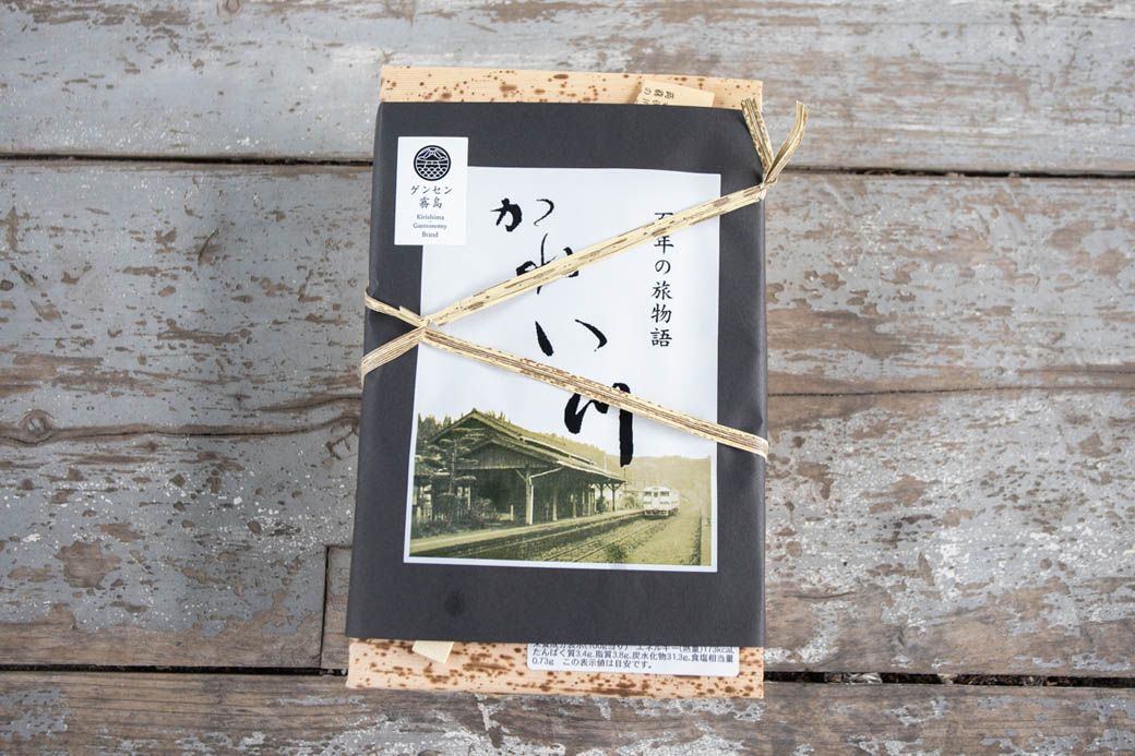 竹皮の弁当箱に、駅舎の写真をプリントした紙を巻いて竹紐で結んである。中には箸とお品書き、お手拭きが入っている。弁当の値段は1800円 （写真：筆者撮影）