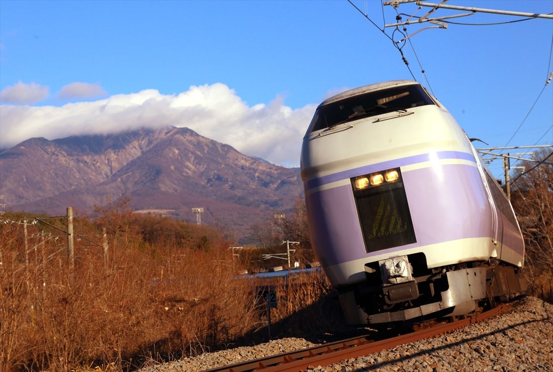 八ヶ岳をバックに車体を傾かせてカーブを快走する「スーパーあずさ」（撮影：南正時）
