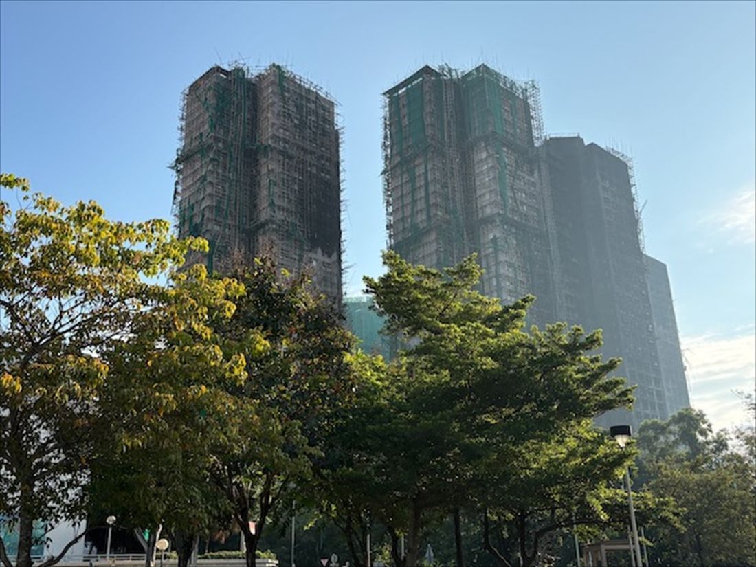 足場と防護ネットで覆われた火災後の高層住宅外壁。火災痕があちこちに見える（筆者撮影）