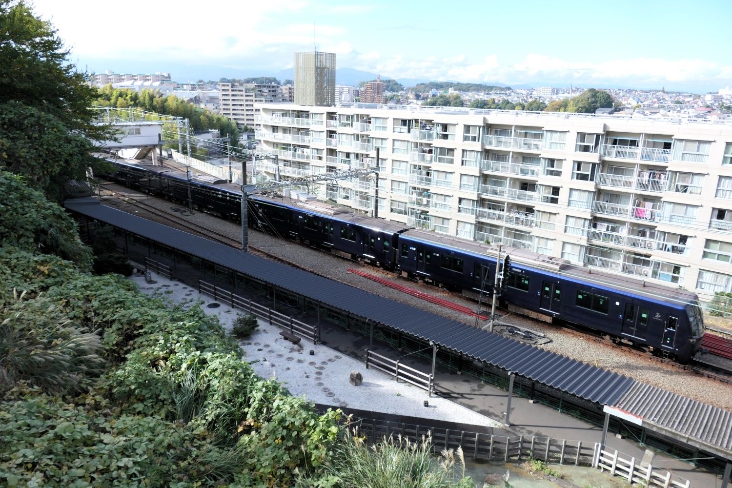 斜面の上の公園から見た東口への通路と電車（記者撮影）