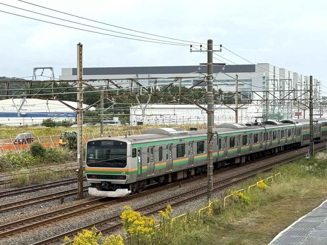 村岡新駅建設予定地付近を走行する東海道線の列車と背後にそびえる「湘南アイパーク」（筆者撮影）