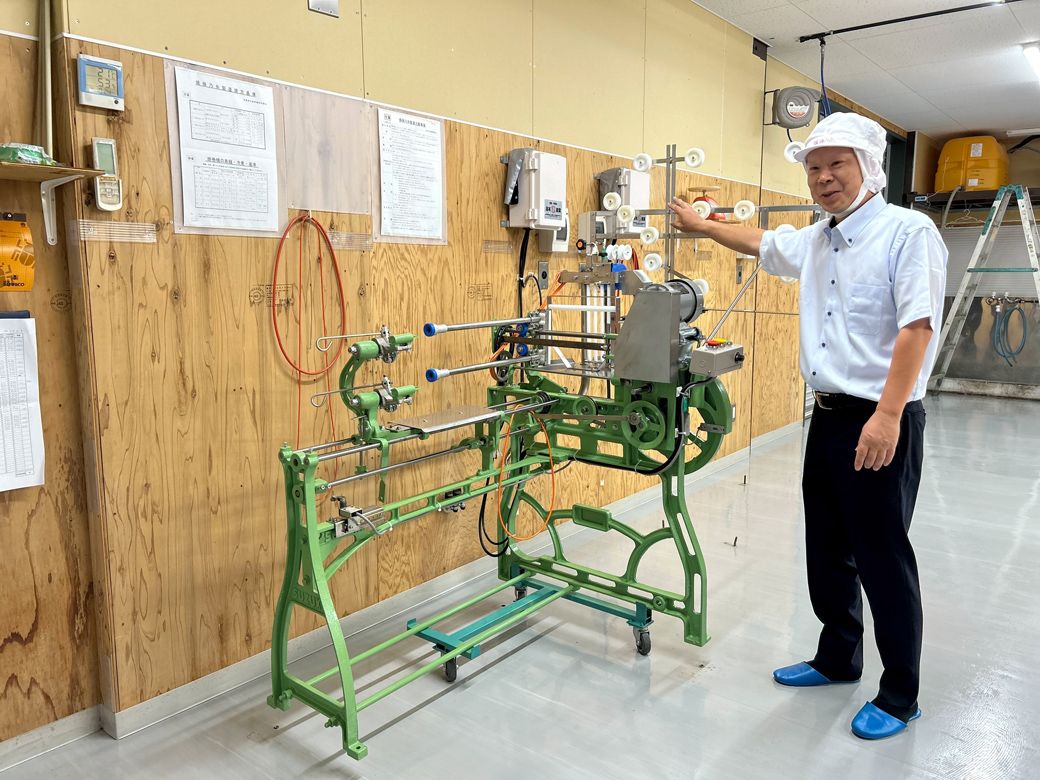 掛巻機（かけばき）の説明をする谷口さん。オフシーズンは工場と機械のメンテナンス期間、ちょうど工場清掃後で床がピカピカだった（筆者撮影）